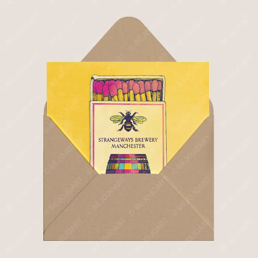 A square greeting card with a bright yellow background and an illustration of a matchbox featuring a bee and the text 'STRANGEWAYS BREWERY MANCHESTER,' tucked inside a brown kraft envelope on a light beige background.