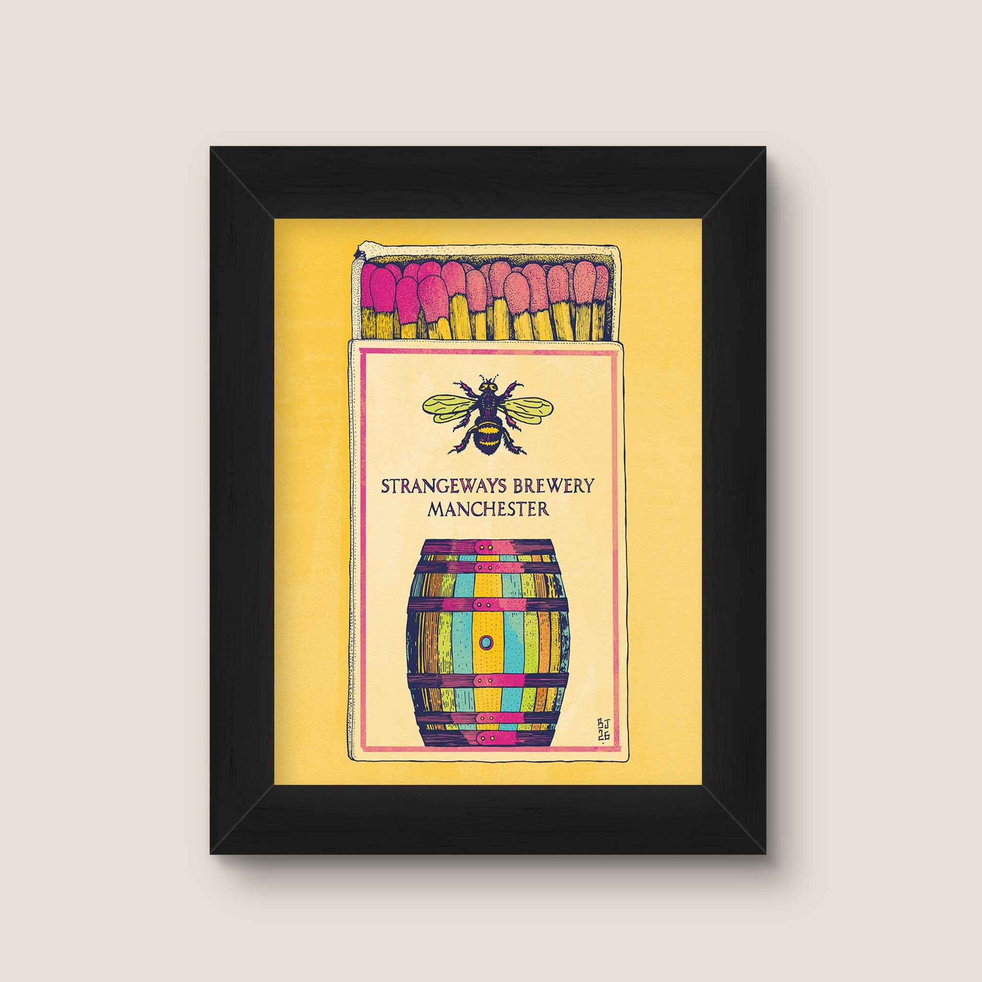 Framed art print featuring a colorful illustration of a matchbox with pink matches, a bee, and a striped barrel, with the text 'Strangeways Brewery Manchester,' shown in a black frame against a light beige wall.