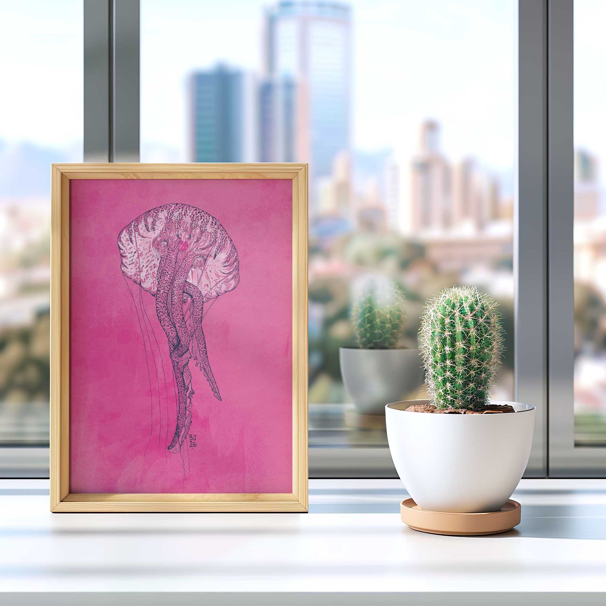 A framed art print featuring a pink background with a detailed black ink sketch of a jellyfish, styled on a windowsill next to a small potted cactus.