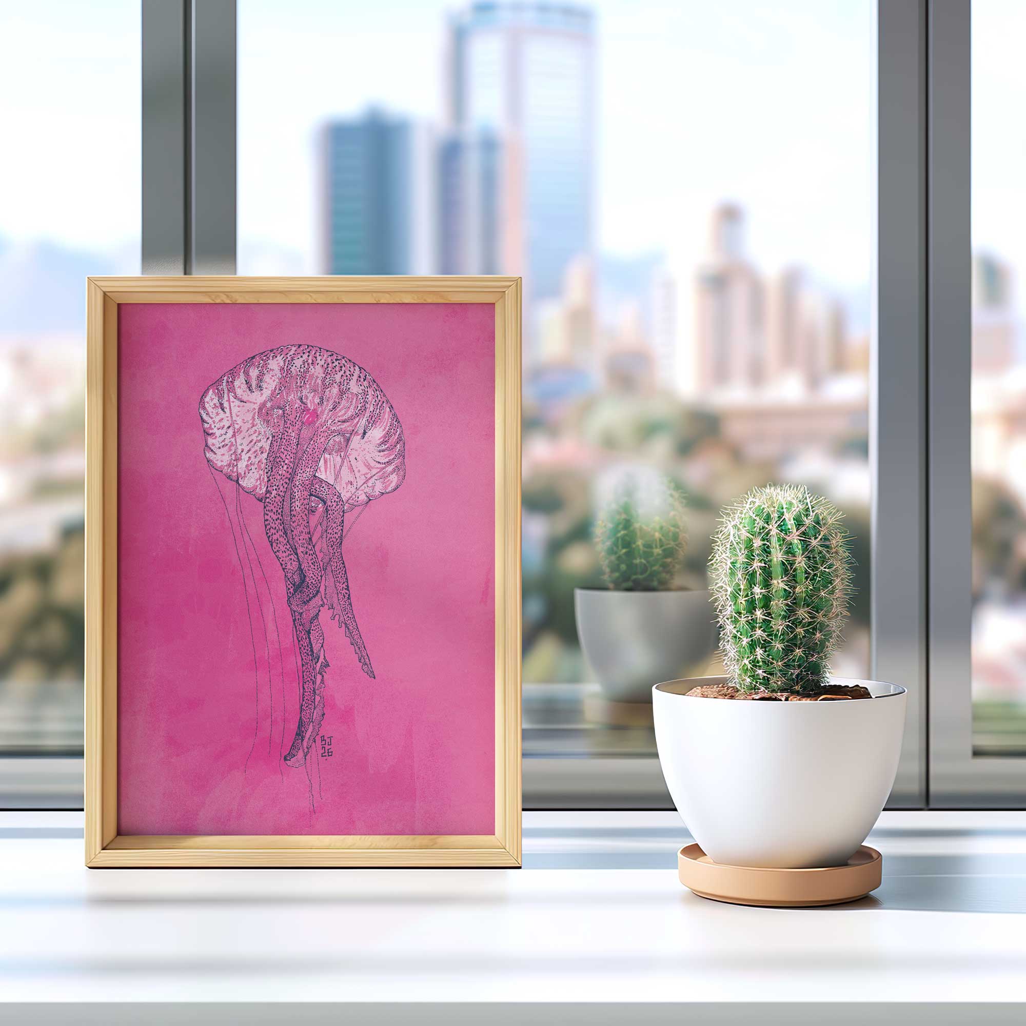 A framed art print featuring a pink background with a detailed black ink sketch of a jellyfish, styled on a windowsill next to a small potted cactus.